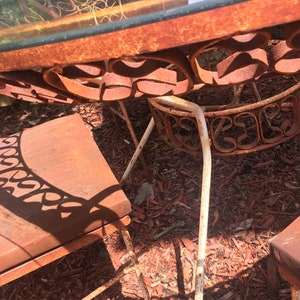 May include: A rusty metal patio table set with a glass top and white painted legs. The table and chairs are sitting on a bed of red wood chips.