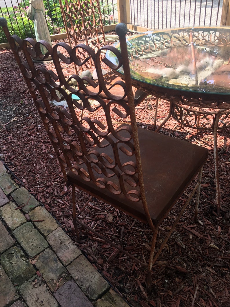 May include: A rusty metal patio chair with a brown cushion. The chair is made of intricate metalwork and has a unique design. The chair is sitting on a bed of brown wood chips.
