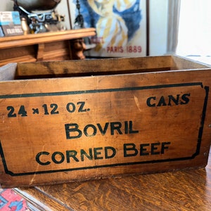 May include: A vintage wooden crate with black lettering that reads "24 x 12 oz. Bovril Corned Beef Cans".