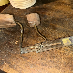 May include: A vintage wooden shoe stretcher with a brass mechanism. The stretcher has two wooden forms and a metal bar with a sliding mechanism.
