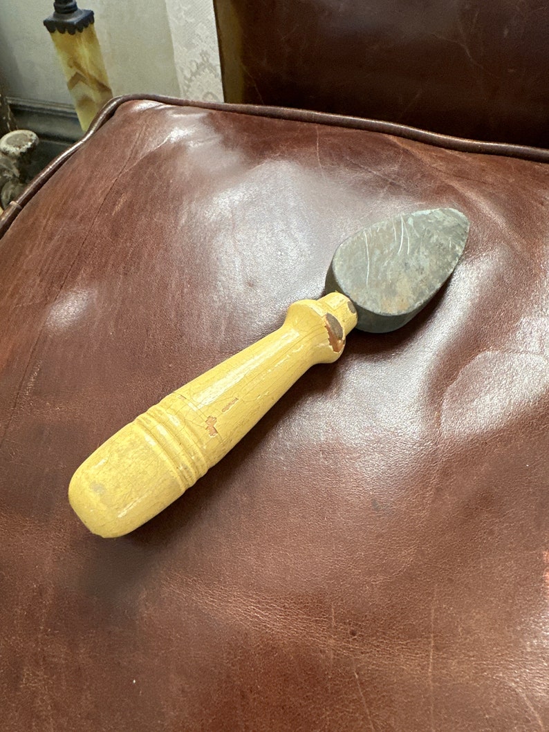 May include: A yellow wooden handled shoe shine brush with a gray stone attached to the end.