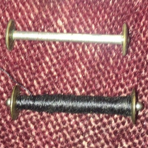 May include: Two spools of thread, one silver and one black, with metal caps on each end.