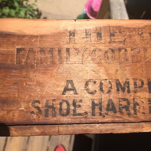 May include: Close-up of a wooden box with the text "The Family Comfort A Complete Shoe Harness" printed on it.
