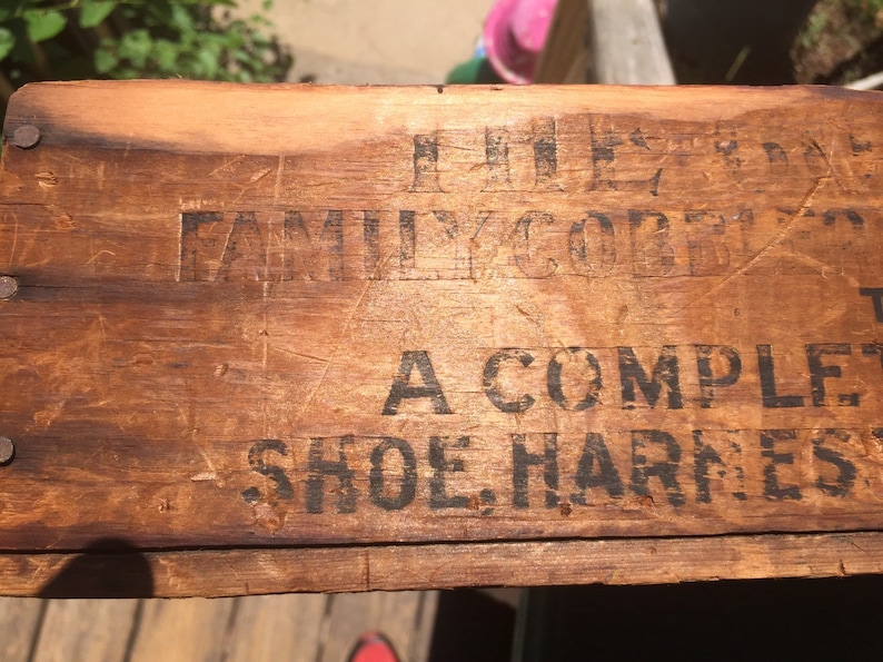May include: Close-up of a wooden box with the text "The Family Comfort A Complete Shoe Harness" printed on it.
