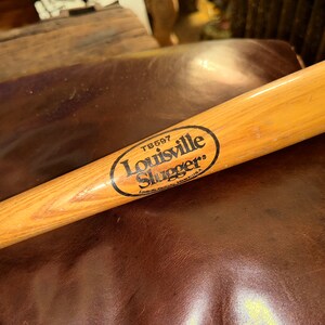 May include: A wooden Louisville Slugger baseball bat with a black oval logo that reads "Louisville Slugger" and "TB697".