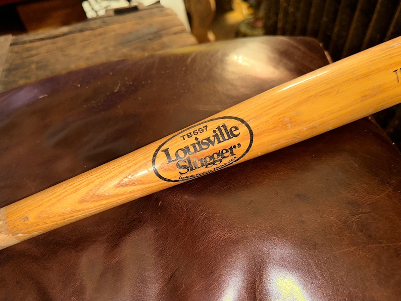 May include: A wooden Louisville Slugger baseball bat with a black oval logo that reads "Louisville Slugger" and "TB697".