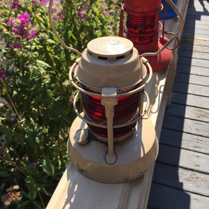 May include: Three antique red and white nautical signal lanterns with glass lenses. The lanterns are on a wooden railing.