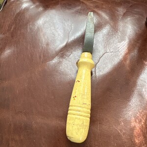 May include: A vintage wooden handled knife with a metal blade. The handle is painted with red and yellow flowers.