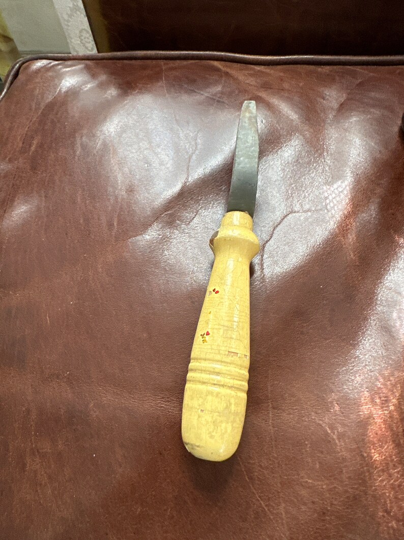 May include: A vintage wooden handled knife with a metal blade. The handle is painted with red and yellow flowers.