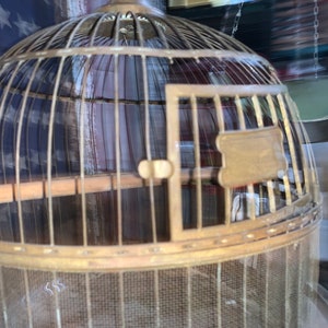 May include: A vintage brass birdcage with a wooden perch and a small door. The cage is round and has a wire mesh bottom.