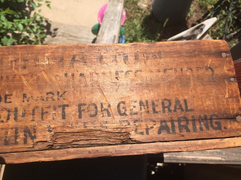 May include: Close-up of a wooden box with black text that reads "TRADE MARK" and "SUIT FIT FOR GENERAL REPAIRING."