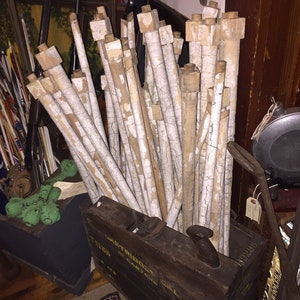 May include: A wooden box filled with a bundle of white painted wooden dowels. The box is labeled "EASTWOOD" and has a yellow and black paint scheme. The dowels are stacked and bundled together.