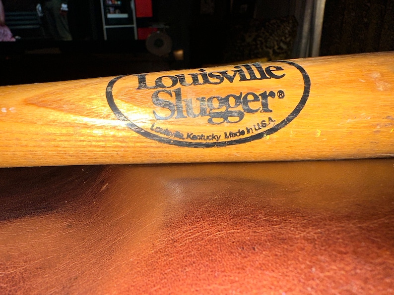 May include: A wooden Louisville Slugger baseball bat with a black oval logo that reads "Louisville Slugger" and "Louisville Kentucky Made in U.S.A."