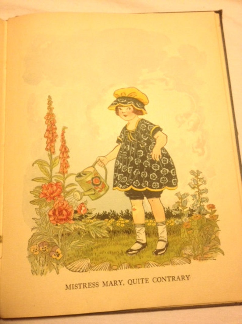 May include: A young girl in a blue and white floral dress and yellow hat waters a garden with a green watering can. The garden has pink flowers, purple flowers, and green leaves. The text "Mistress Mary, Quite Contrary" is printed below the image.