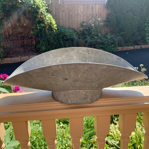 May include: A large, silver-colored metal planter shaped like a trough. The planter is sitting on a wooden railing.
