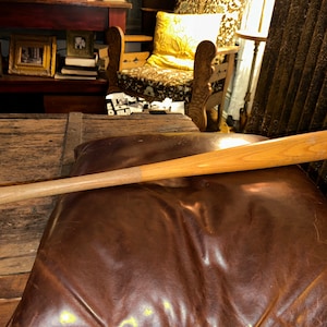 May include: A wooden baseball bat with a natural finish. The bat is lying on a brown leather surface.