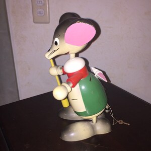 以下が含まれることがあります： ヴィンテージの木製マウスのおもちゃ。マウスは灰色の体、ピンクの耳をしており、赤と緑の衣装を着ています。黄色い棒を持ち、尻尾には鍵が付いています。ノスタルジックなアイテムです。