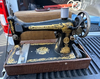 May include: A vintage black Singer sewing machine with gold accents and intricate designs. The machine is in a brown leather case with a crocodile pattern.