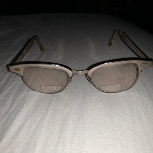 May include: Silver-toned glasses with a gold accent on the frame. The glasses have a classic, vintage style.