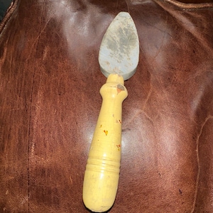 May include: A gray sharpening stone with a wooden handle. The handle is painted yellow with red and orange accents.