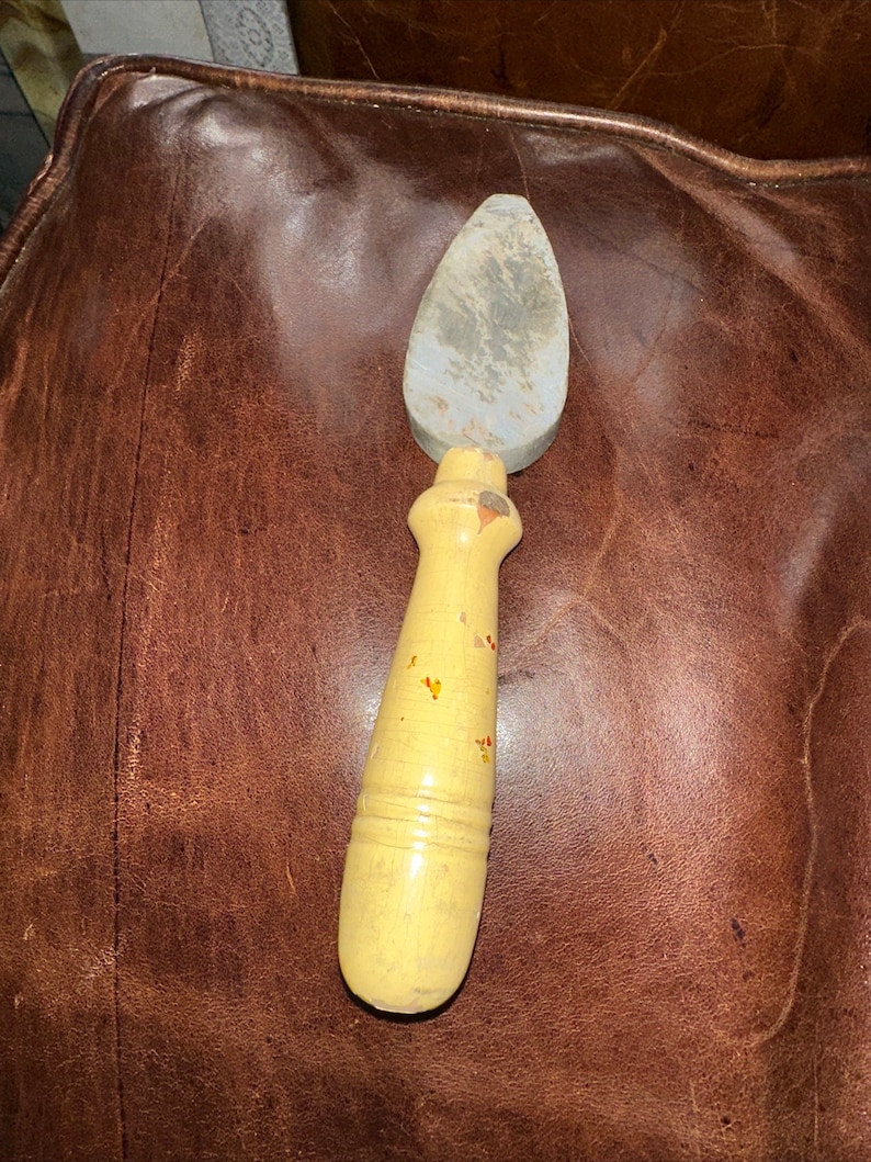 May include: A gray sharpening stone with a wooden handle. The handle is painted yellow with red and orange accents.
