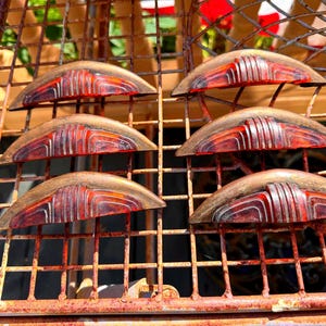 May include: A set of six semi-circular drawer pulls featuring a metallic bronze-toned finish and a translucent, deep red center inlay with raised, curved lines. Each handle has a wide, arched shape with a flat base and a decorative, ribbed design.
