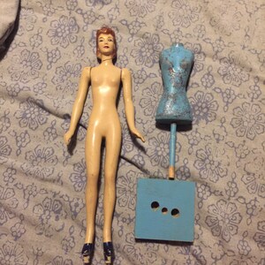 May include: A vintage wooden doll with a painted face and blue shoes. The doll is standing next to a blue wooden dress form with a stand.