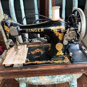 May include: A vintage black Singer sewing machine with gold accents and a wooden base. The machine has a white thread spool and a foot pedal.