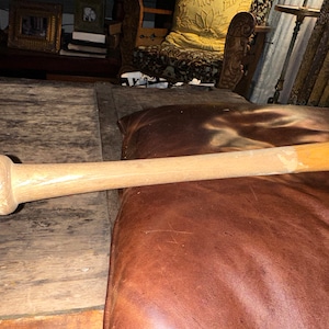 May include: A wooden baseball bat with a natural finish. The bat is lying on a brown leather surface.