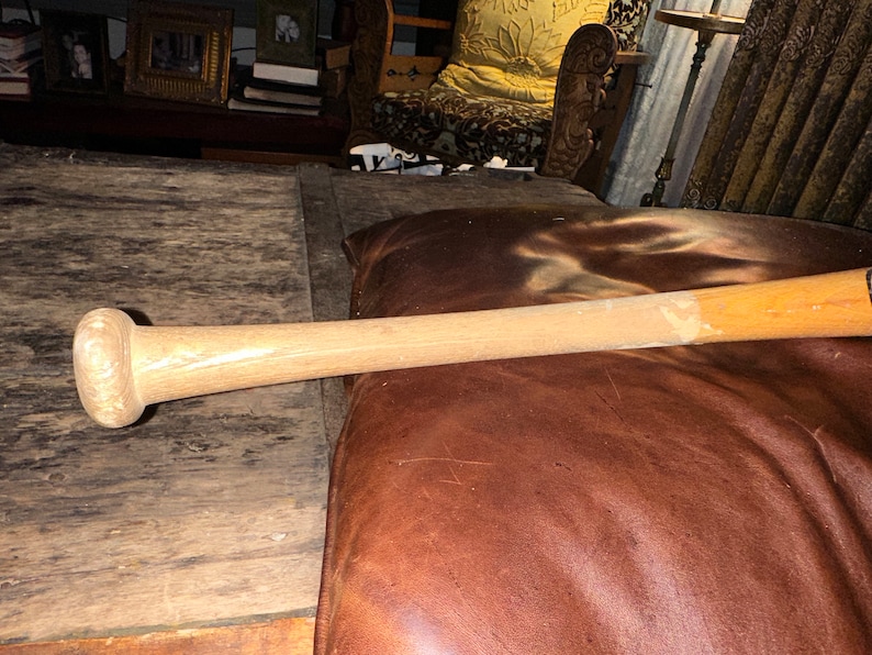 May include: A wooden baseball bat with a natural finish. The bat is lying on a brown leather surface.
