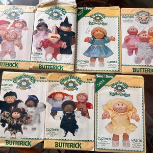 May include: A collection of vintage Cabbage Patch Kids sewing patterns. The patterns feature illustrations of the dolls in various outfits. The Butterick patterns are in various colors, including yellow, white, and blue.