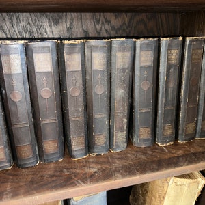 May include: A set of ten brown leather-bound books titled "History of the World" by John Clark Ridpath. Each book has a gold-colored title and a gold-colored illustration of a torch on the front cover. The books are arranged in order from volume one to volume ten on a wooden shelf.