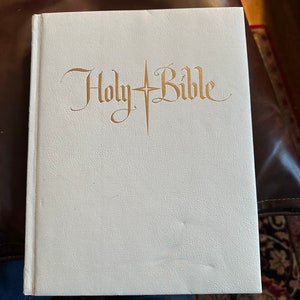 May include: A white leather-bound Holy Bible with gold lettering.