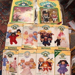 May include: A collection of ten Cabbage Patch Kids sewing patterns by Butterick and See & Sew, featuring yellow and white packaging with illustrations of dolls wearing various outfits, including western wear, formal dresses, and casual clothing.