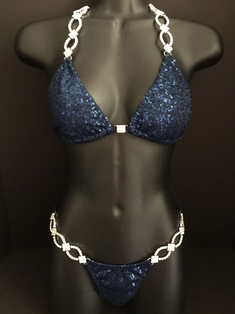 May include: A navy blue sequined bikini with crystal embellishments on the straps and sides. The bikini top has a triangle shape and the bottom is a thong style.