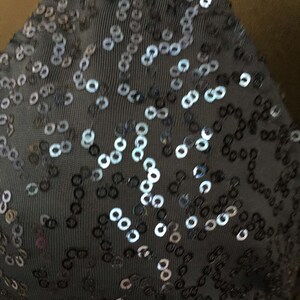 May include: Close-up of a dark gray fabric with silver and black sequins arranged in a pattern.