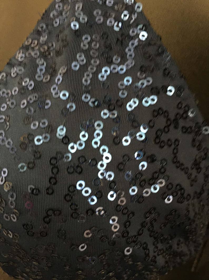 May include: Close-up of a dark gray fabric with silver and black sequins arranged in a pattern.