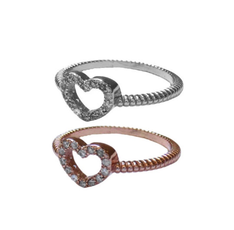 May include: Two heart-shaped rings with a twisted band. One ring is silver with a clear heart, and the other is rose gold with a clear heart.
