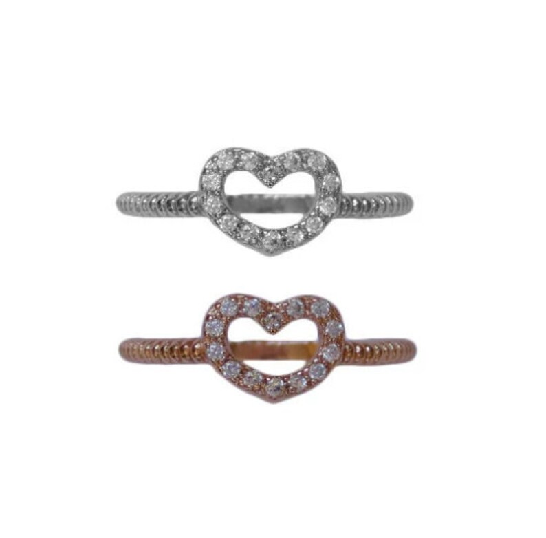 May include: Two heart-shaped rings with a clear stone setting. The ring on top is silver, and the ring on the bottom is rose gold.