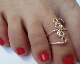 May include: A silver toe ring with a swirling design. The ring is worn on a foot with red nail polish.