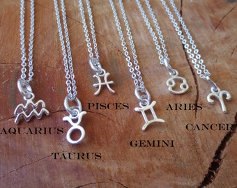 May include: Silver-toned necklaces with zodiac sign pendants. The image displays several necklaces, each with a different astrological symbol, including Aquarius, Taurus, Pisces, Gemini, Aries, and Cancer. The pendants are suspended from delicate chains.