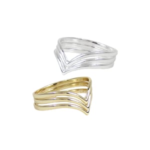 May include: Two rings, one silver and one gold, each with a layered V-shaped design. The rings are set against a white background, showcasing their sleek and modern aesthetic. The gold ring has a warm, lustrous finish.