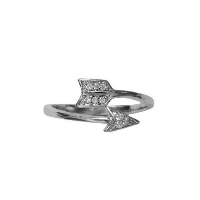May include: A silver-toned ring featuring an arrow design. The arrowheads are embellished with small, clear gemstones. The ring has a delicate, open design, with the arrowheads pointing in opposite directions. The ring is set against a white background.