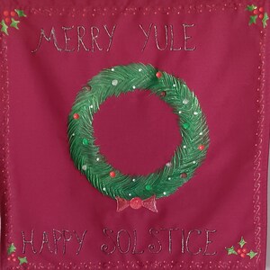 Pode incluir: Bandeira de tecido bordô com as palavras "MERRY YULE" e "HAPPY SOLSTICE" bordadas em prata. Uma grinalda verde com detalhes vermelhos e verdes está no centro. A bandeira tem uma borda decorativa com azevinho.