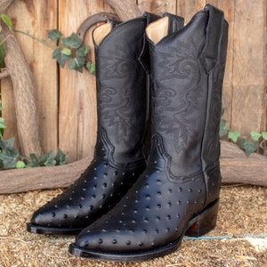 May include: A pair of black ostrich leather cowboy boots with intricate stitching on the shaft. The boots have a pointed toe and a stacked heel.