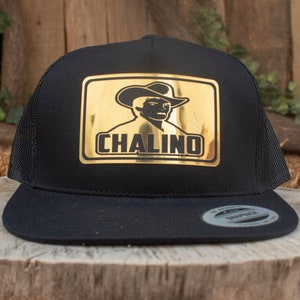 May include: Black trucker hat with a gold patch featuring a silhouette of a person wearing a cowboy hat and the word "CHALINO".