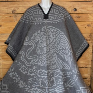 May include: Gray wool poncho with a white embroidered design of an eagle and a cactus. The poncho has a black trim around the neckline and a fringe around the bottom.