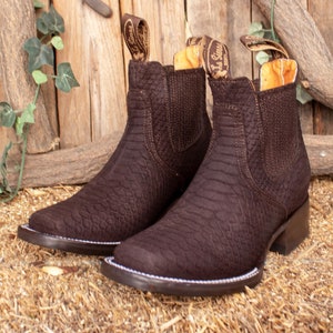 Op de afbeelding: Een paar bruine leren enkellaarsjes met een textuur, geëmbosseerd afwerking. De laarzen hebben een slip-on ontwerp en een lage hak.