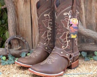 May include: A pair of brown leather cowboy boots with floral embroidery and a strap across the ankle. The boots have a pointed toe and a low heel.