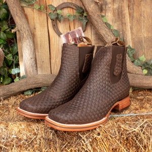 以下が含まれることがあります： 編み込み模様の入った茶色の革製のアンクルブーツのペア。ブーツは丸みを帯びたつま先と低いヒールを持っています。